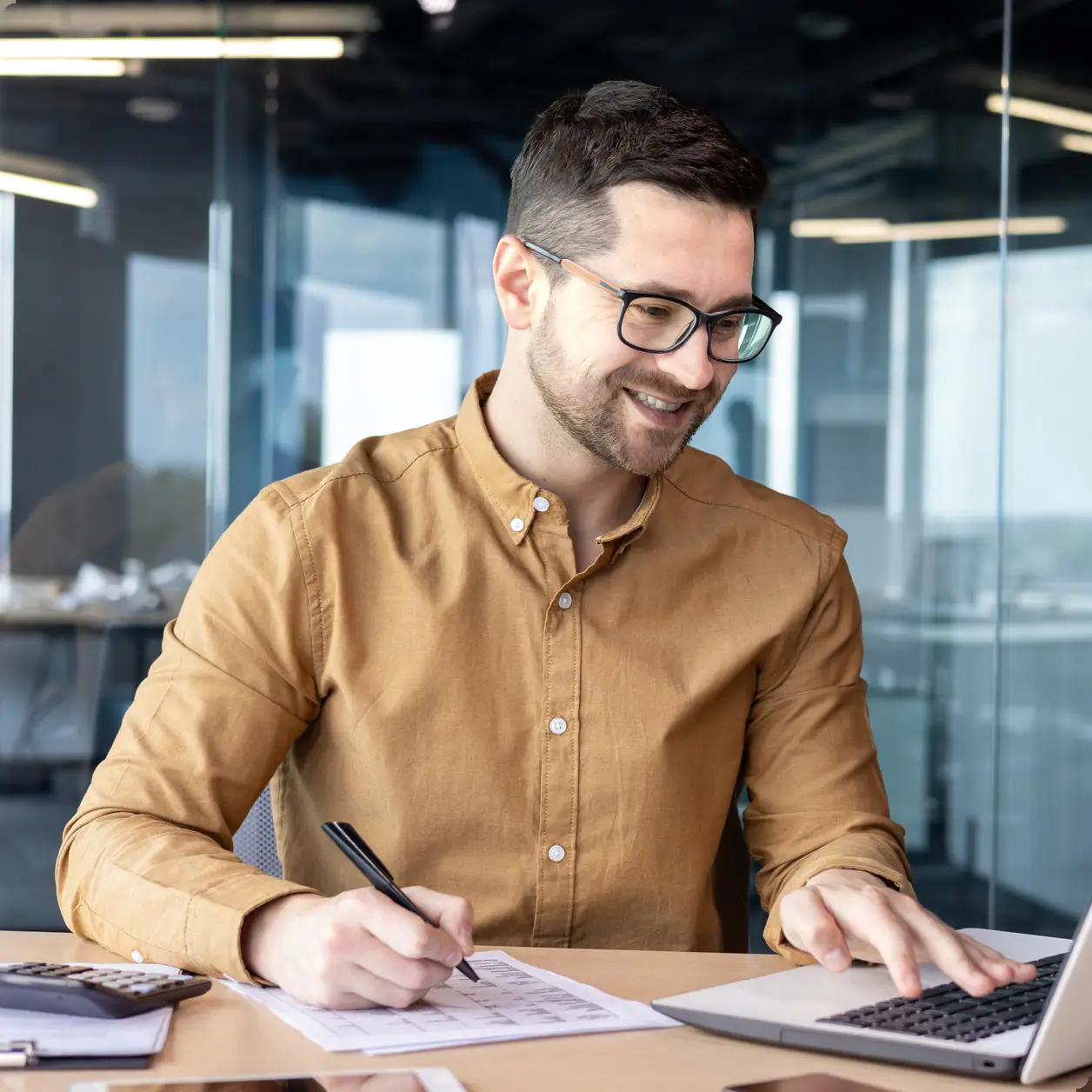 Man writing up records at a desk beside a laptop