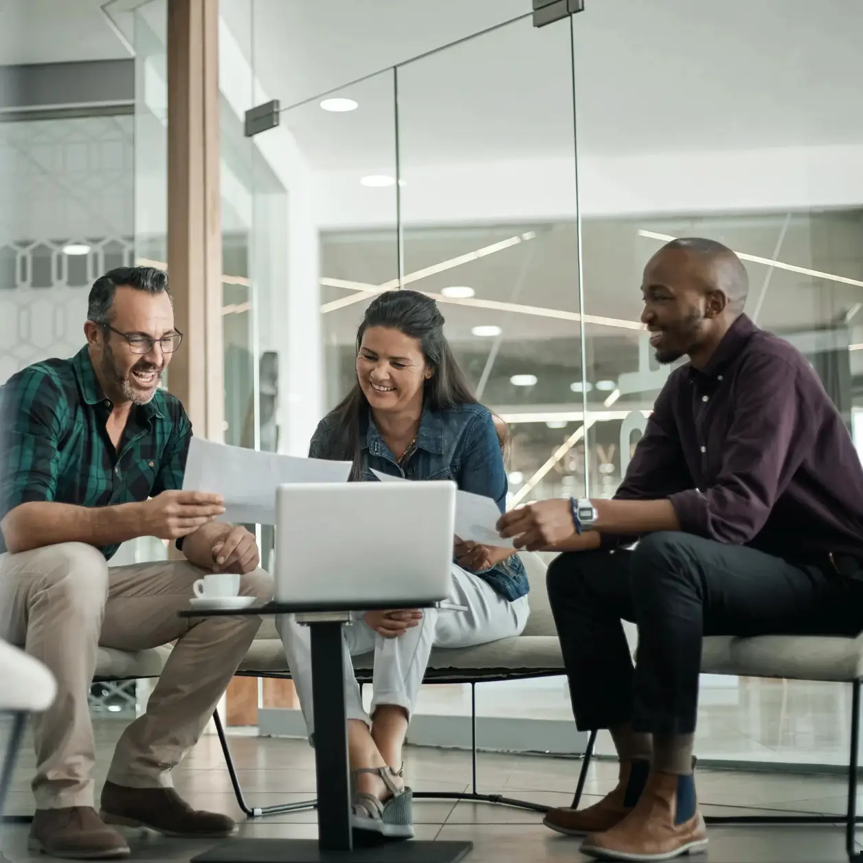 Three people in an informal business meeting in a glass-walled office