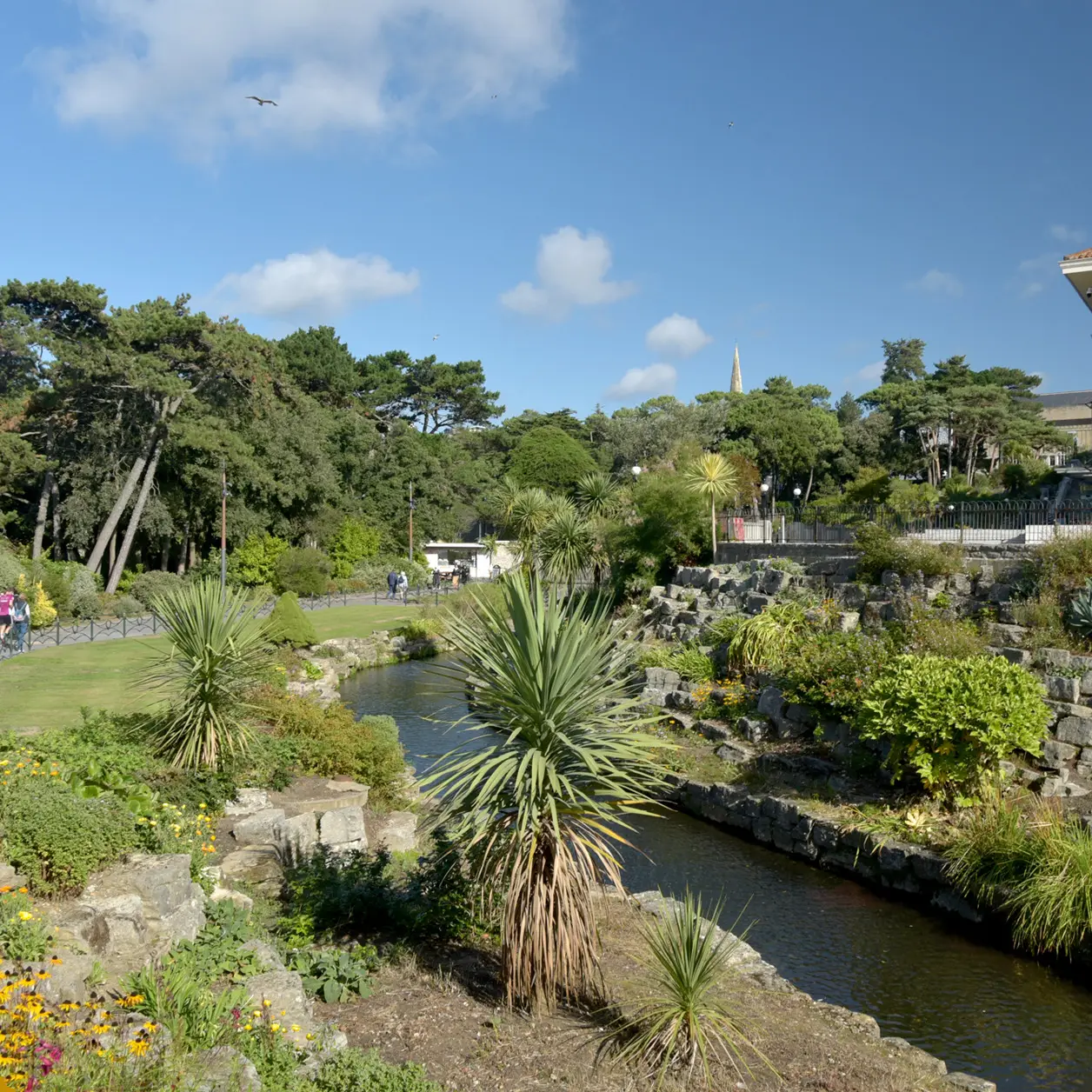 Landscaped gardens with a stream and palm trees under a blue sky